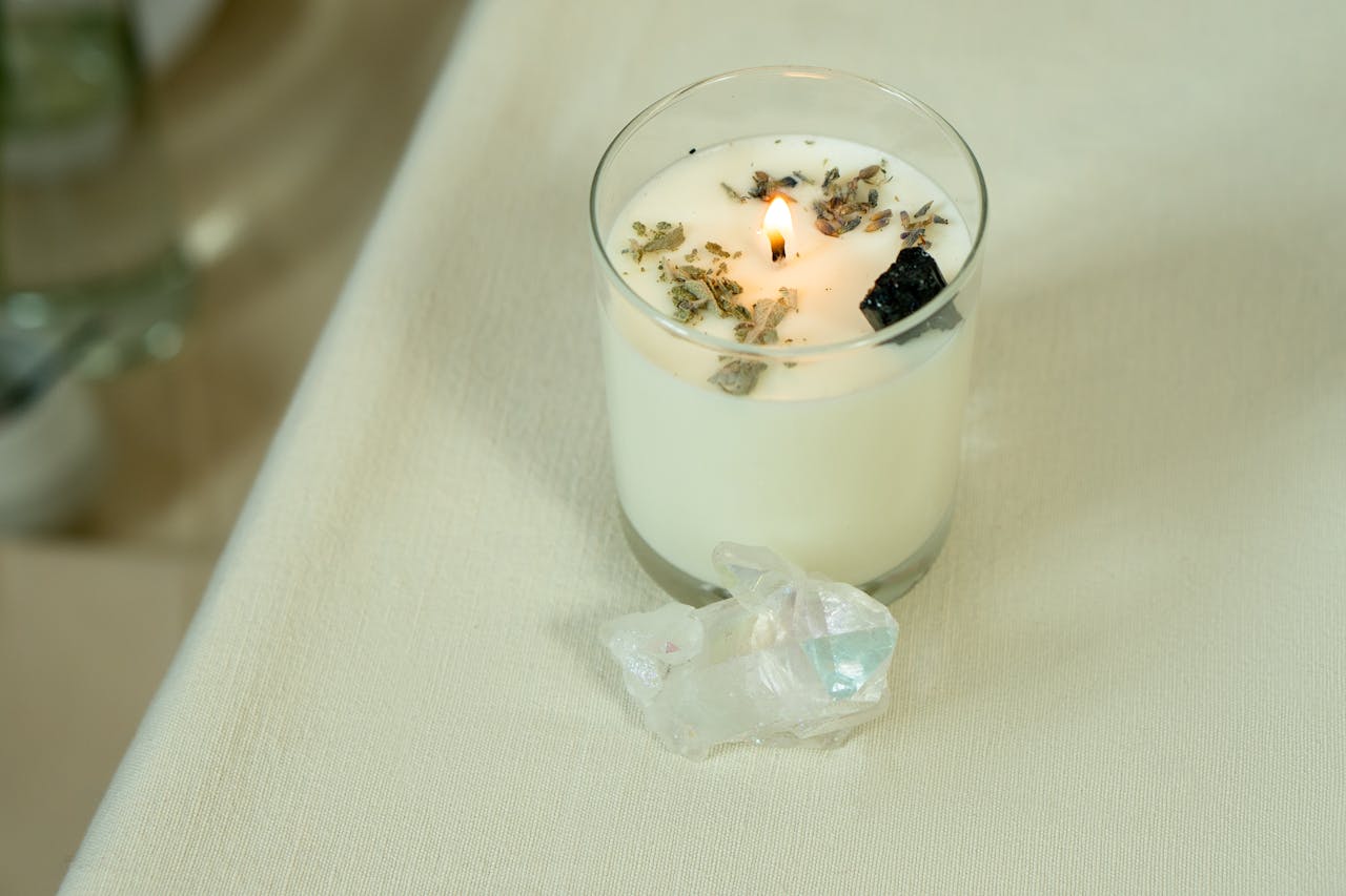 Lit aromatherapy candle with herbs and crystals for relaxation and healing.